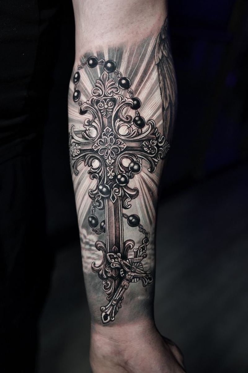 Black-and-gray realism ornate cross and rosary tattoo on a forearm